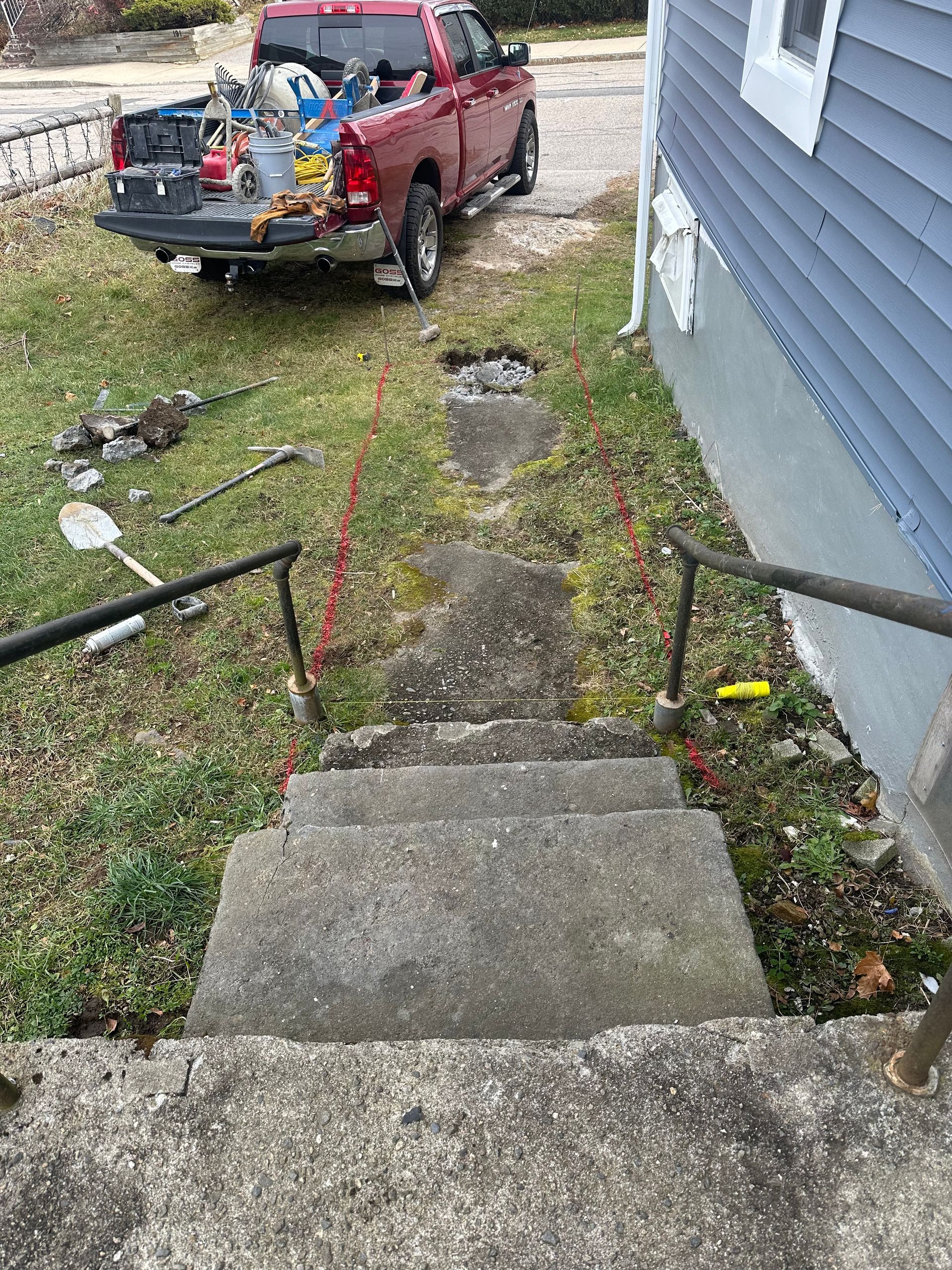 Front steps and walkway beside a house, with a red pickup truck parked in the yard ahead.