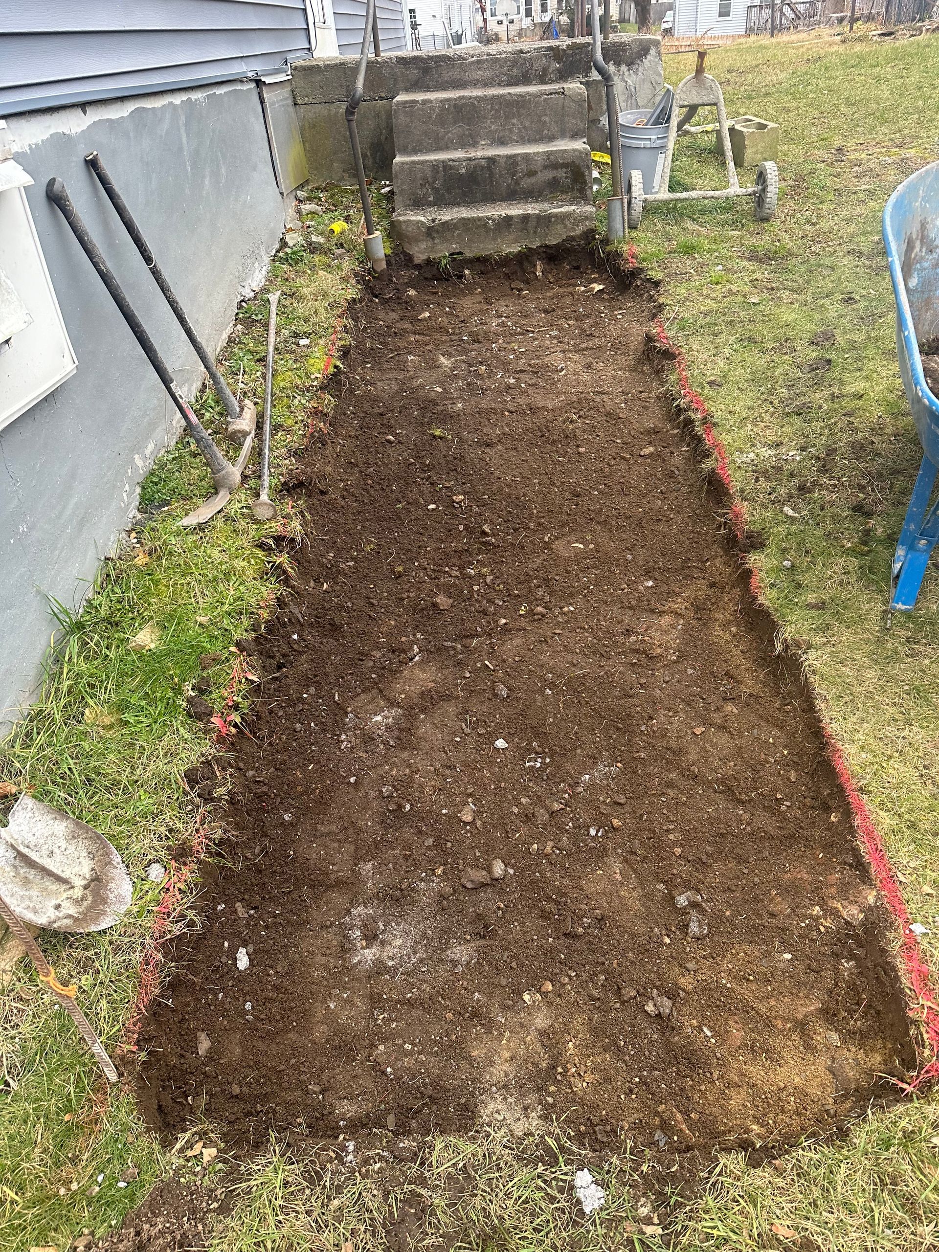 Freshly cleared rectangular garden bed beside a house, bordered with red edging and a stone step at the end.