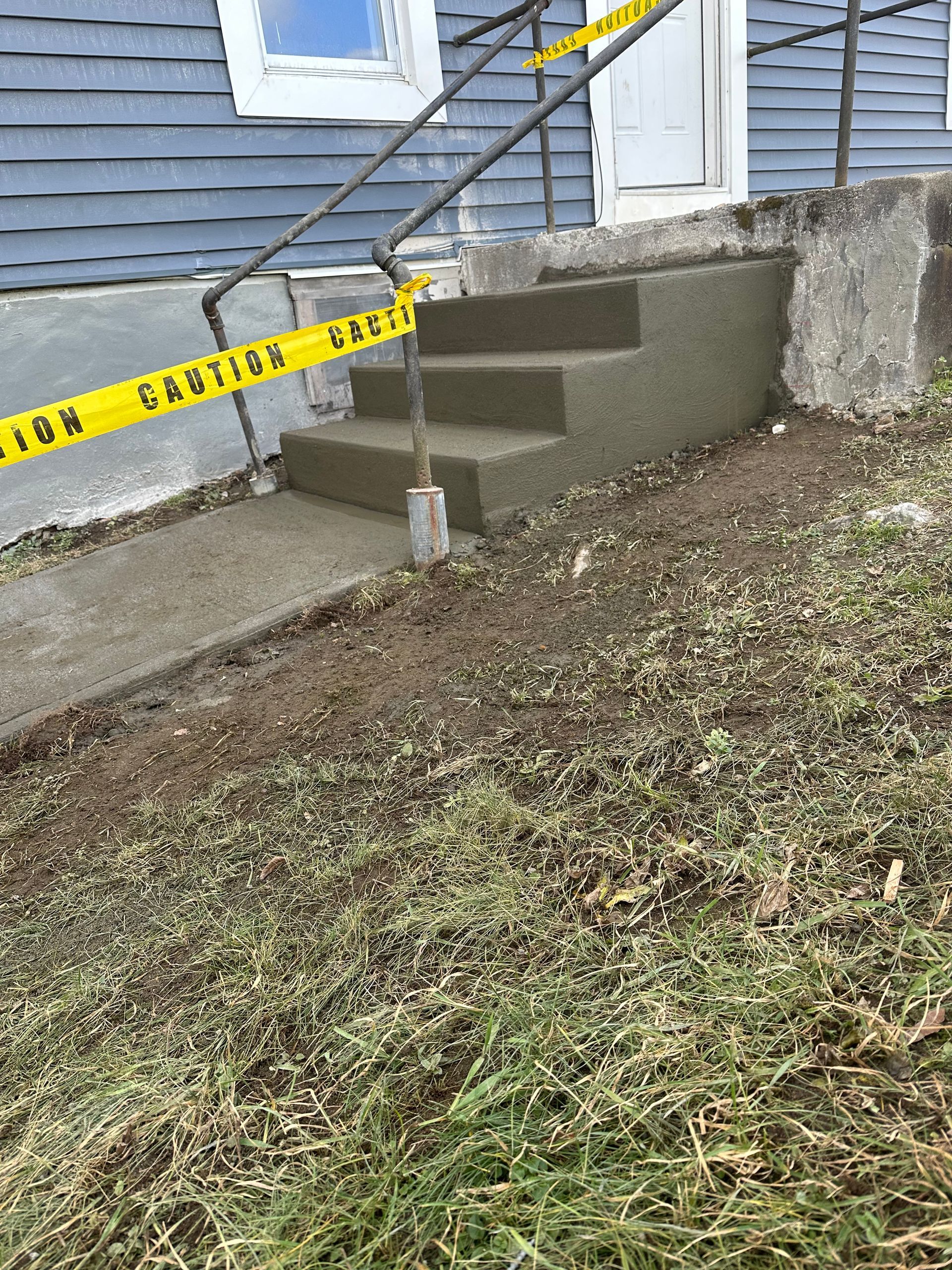 Caution tape blocking front steps to a house beside a grassy slope and retaining wall