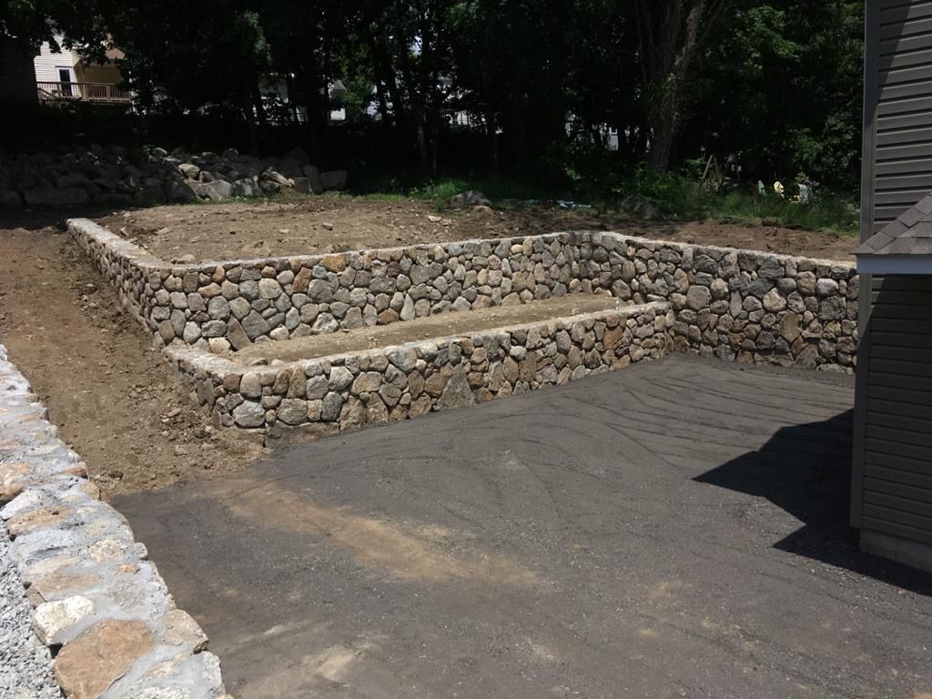 Stone retaining wall around a paved driveway in a shaded yard