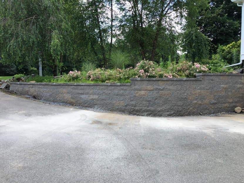 Curved garden wall with shrubs and trees beside a paved path
