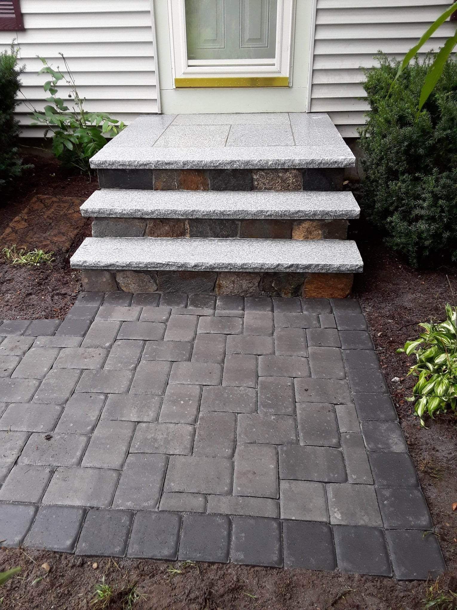Front entry with granite steps leading to a white house, bordered by mulch and a gray paver walkway.