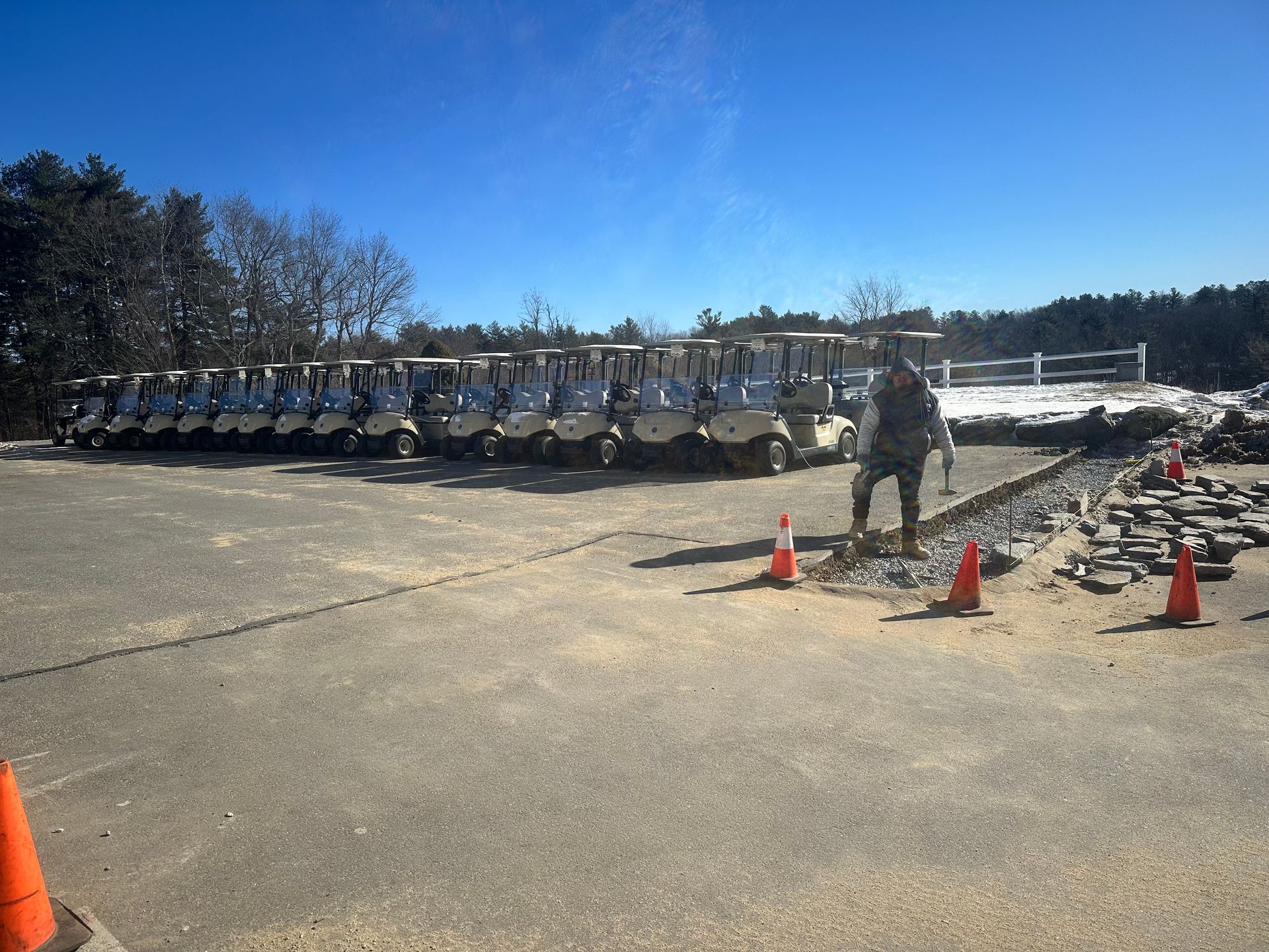 Row of white utility trucks parked on a sunlit lot, with cones and a worker nearby.