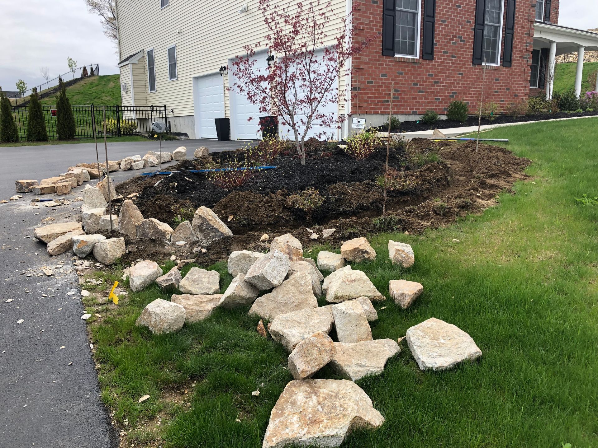Rock border and mulch bed beside a house, with scattered rocks on the grass and driveway.