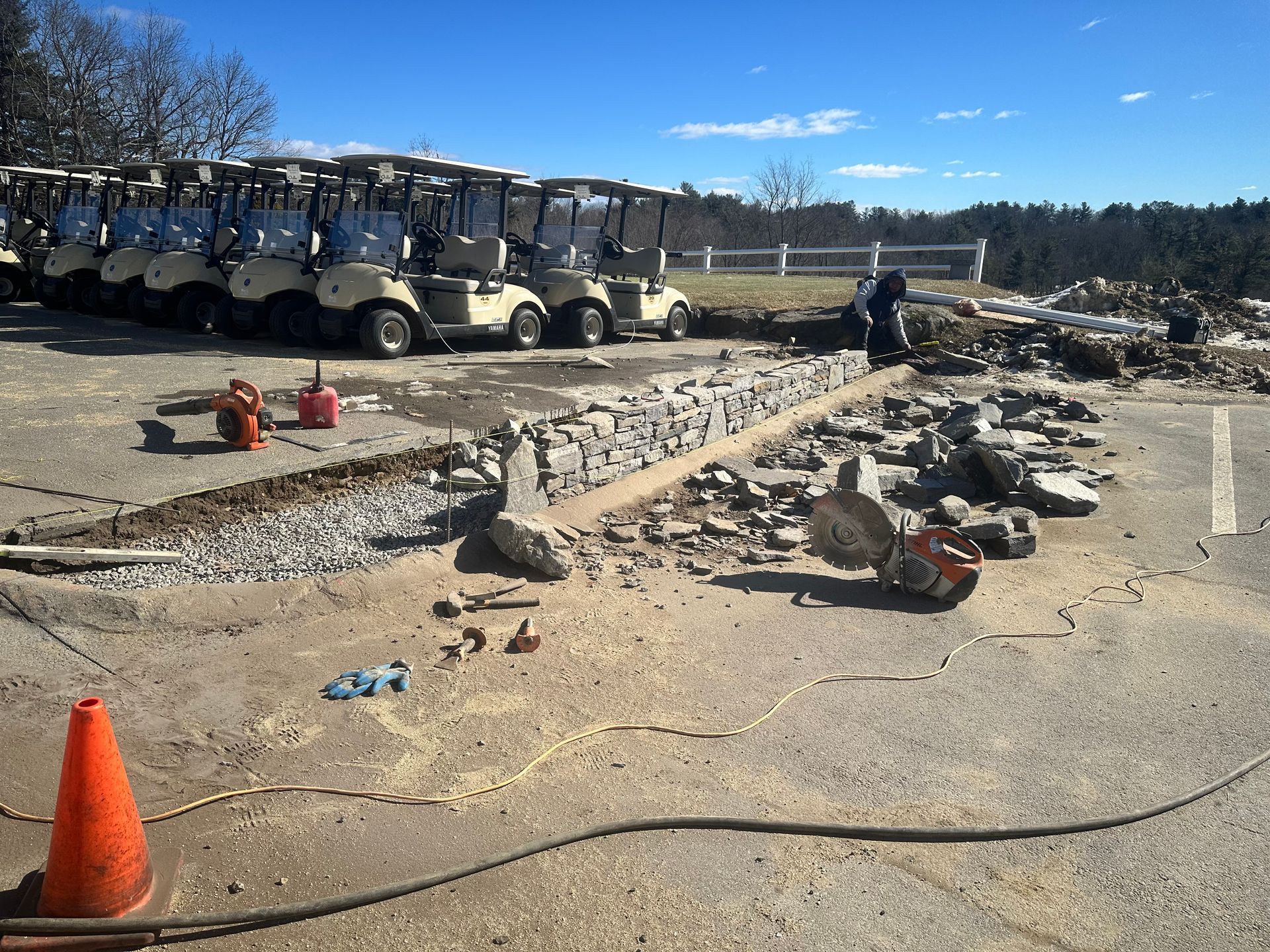 Golf carts lined up beside a rocky construction site under a clear blue sky.