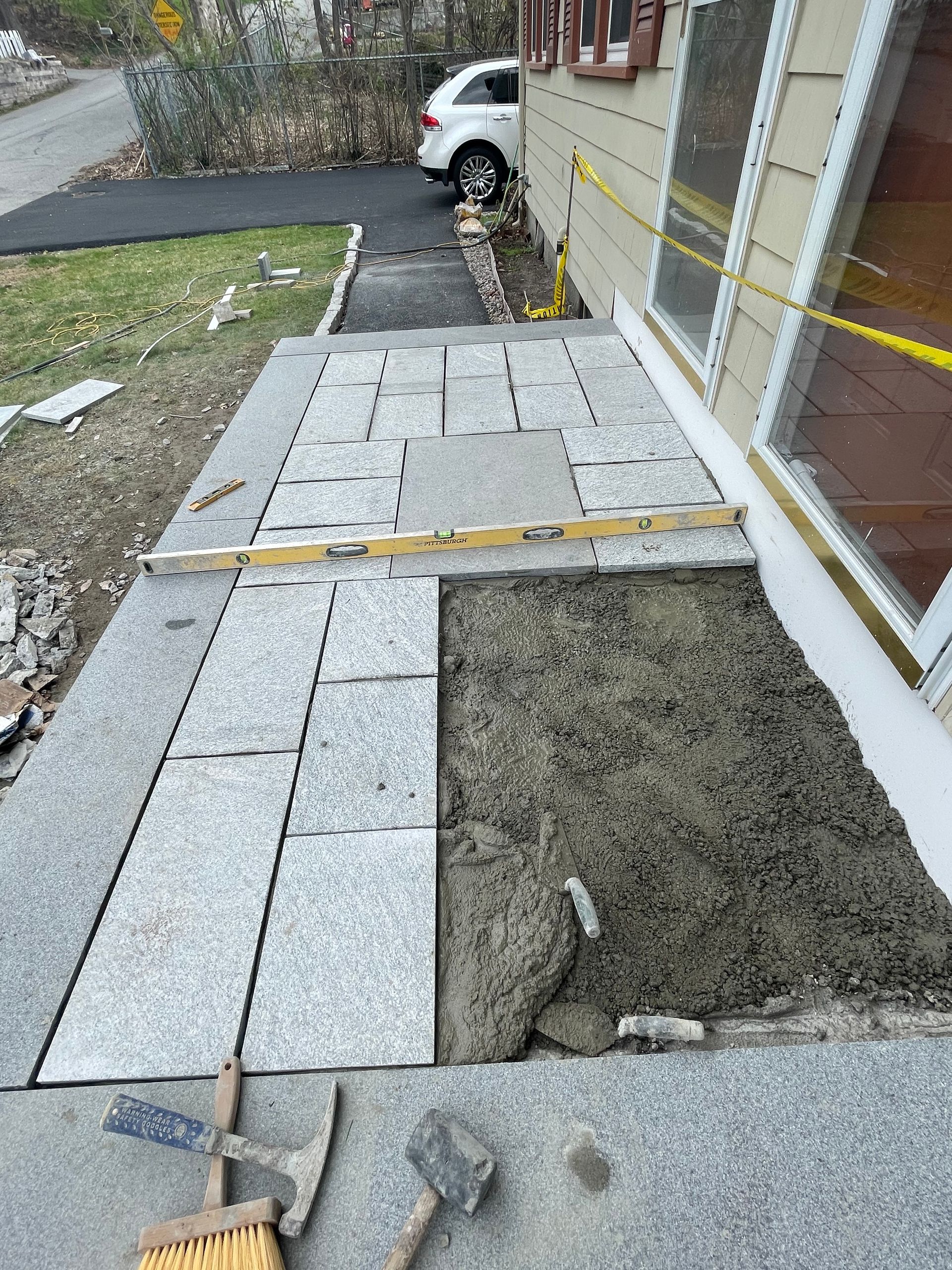 Residential walkway under construction with pavers, gravel, and a parked car beside the house.