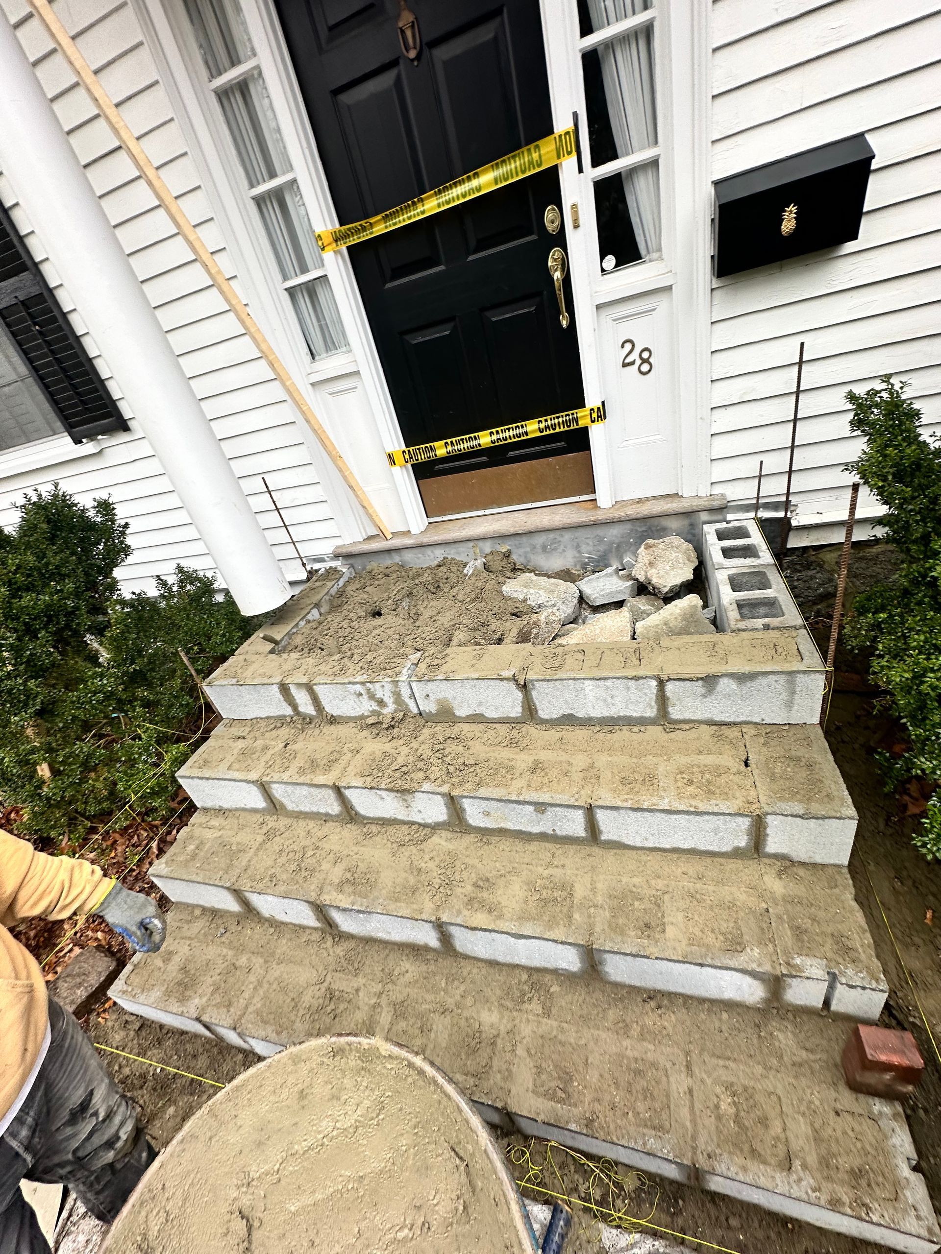 Broken concrete steps leading to a black front door, marked with yellow caution tape at a house entrance