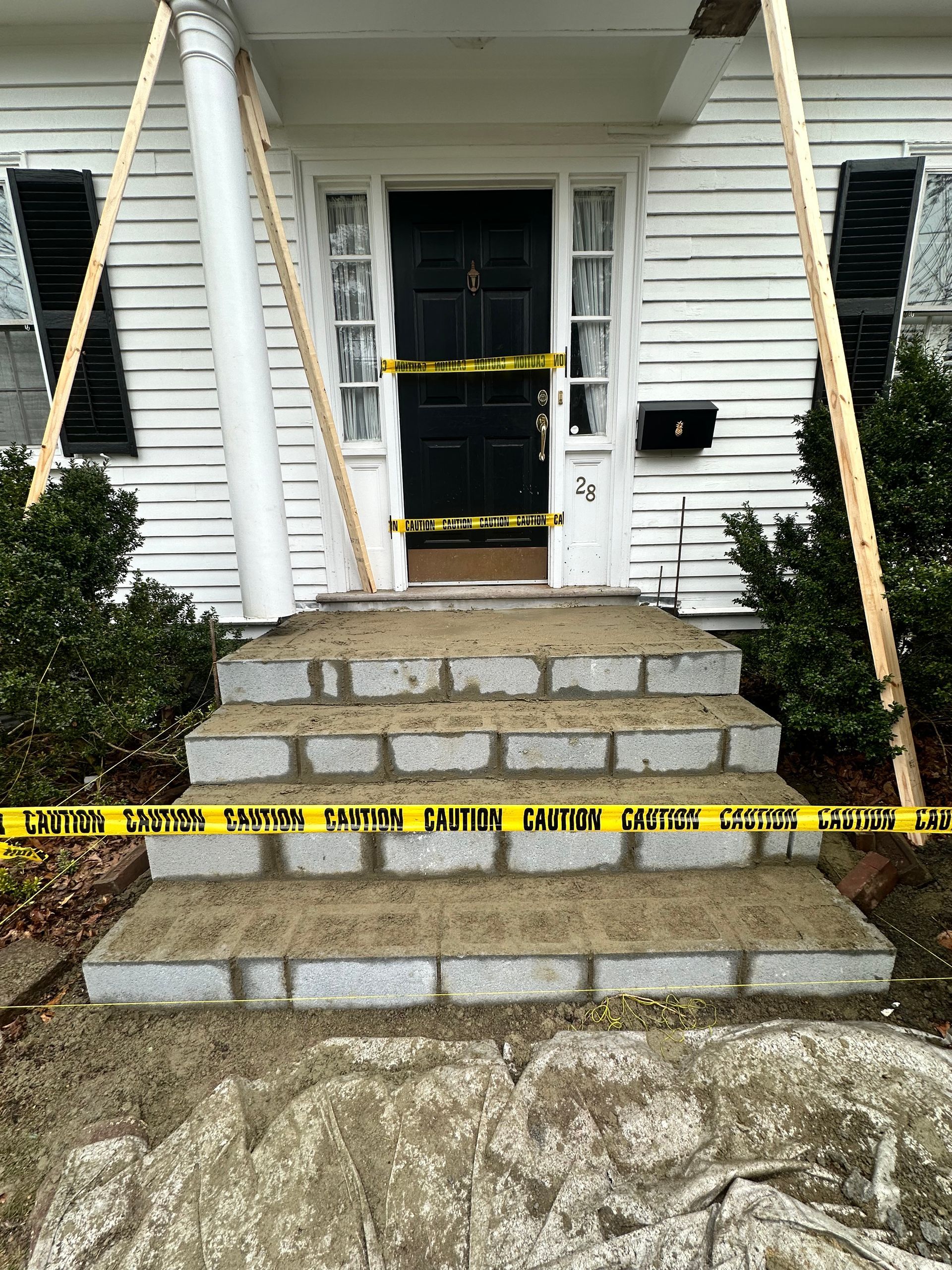 Caution-taped front steps and doorway of a white house, indicating restricted entry after damage or repair.