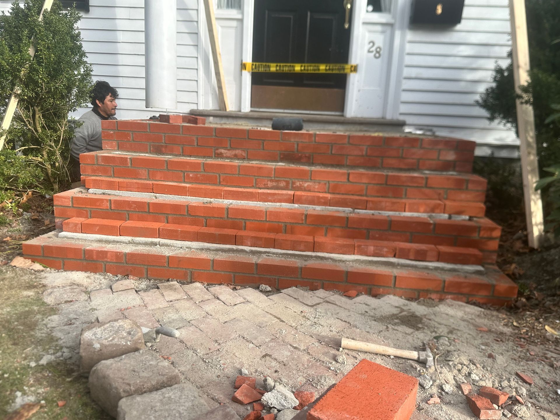 Partially built brick front steps on a house, with loose bricks and rubble in the foreground.