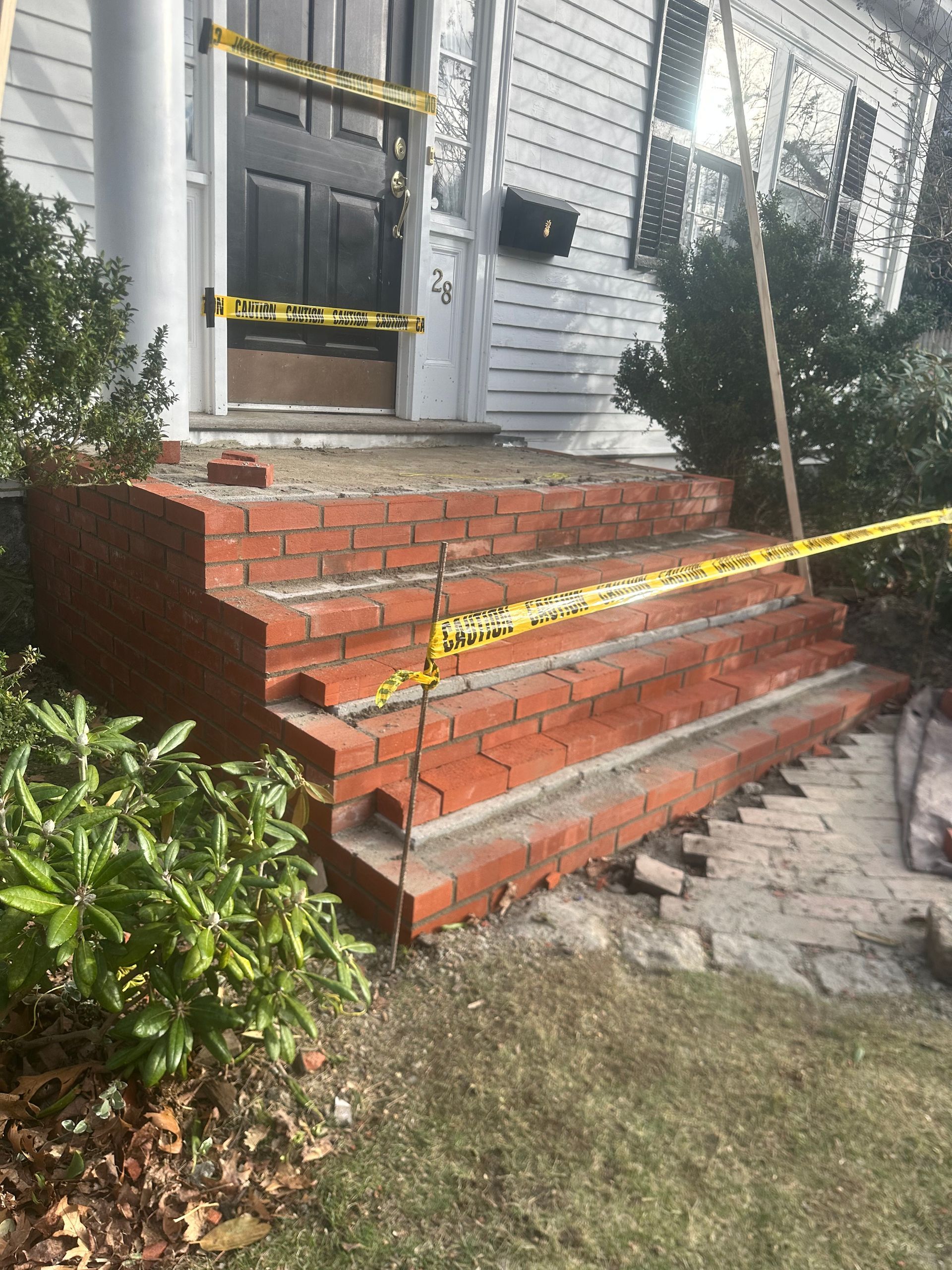 Front porch brick steps and entry door cordoned off with yellow caution tape due to damage.