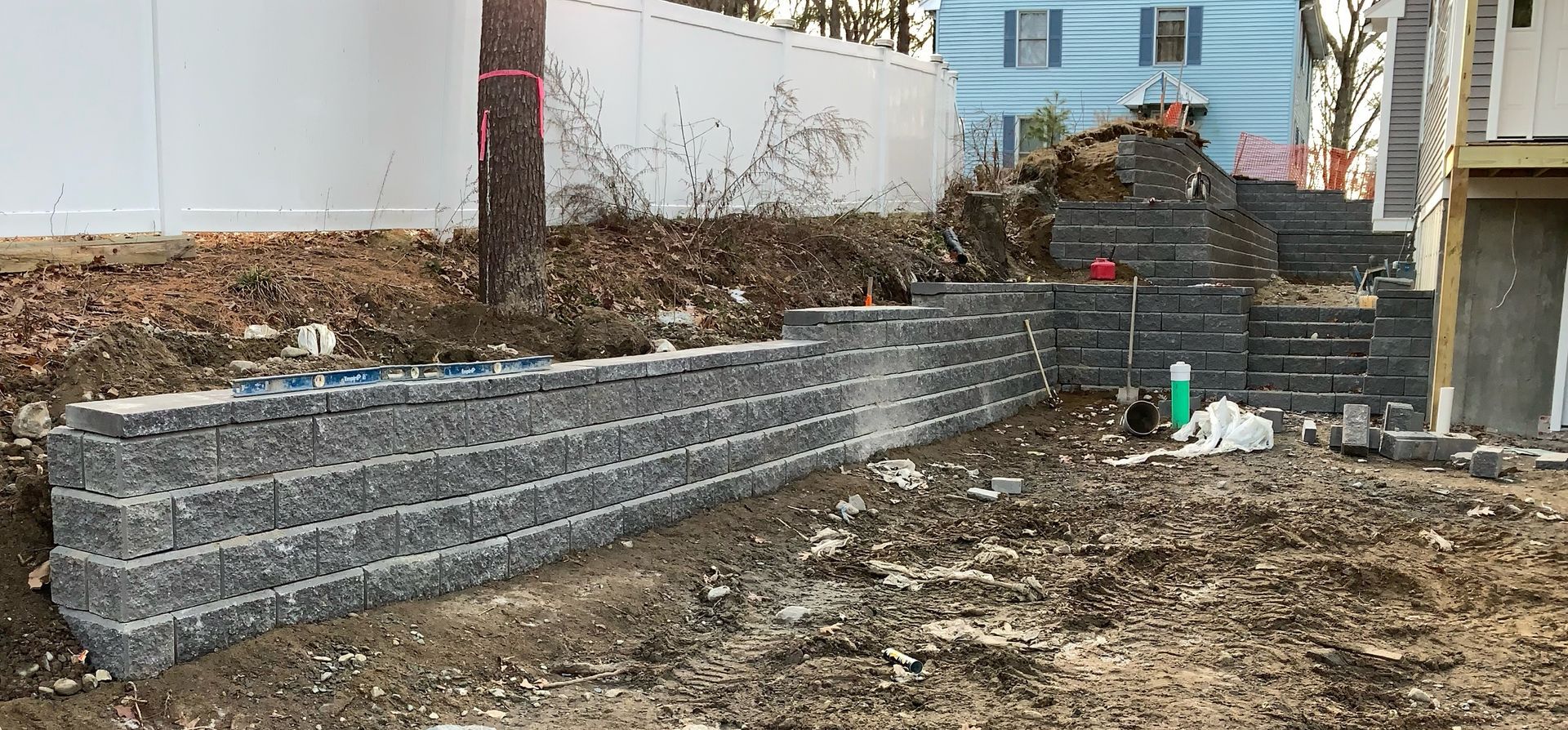 Retaining wall under construction beside a house, with excavated dirt and a few building materials.