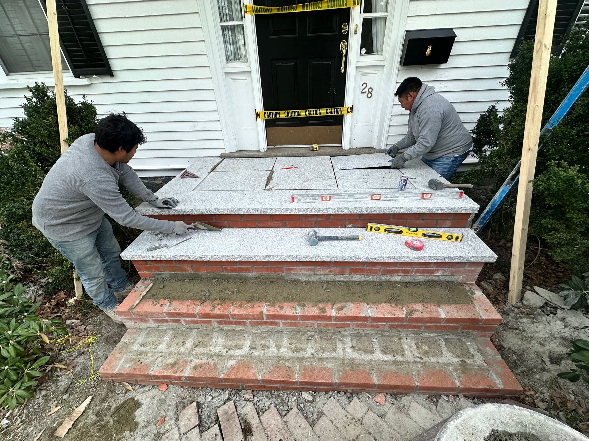 Two workers moving white panels up brick steps to a house entrance under construction