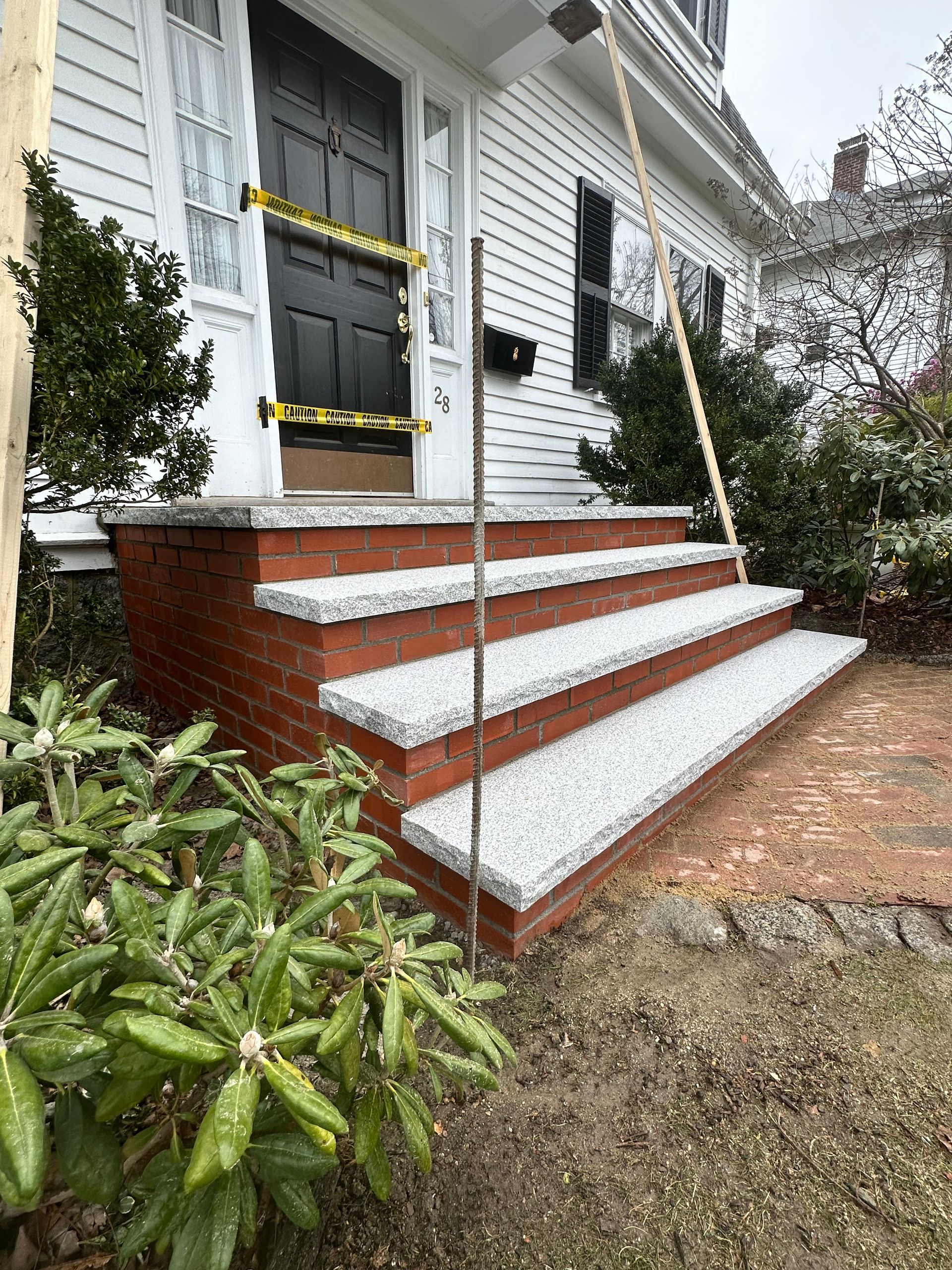 Front steps to a white house with red brick risers and a black door, viewed from a garden path