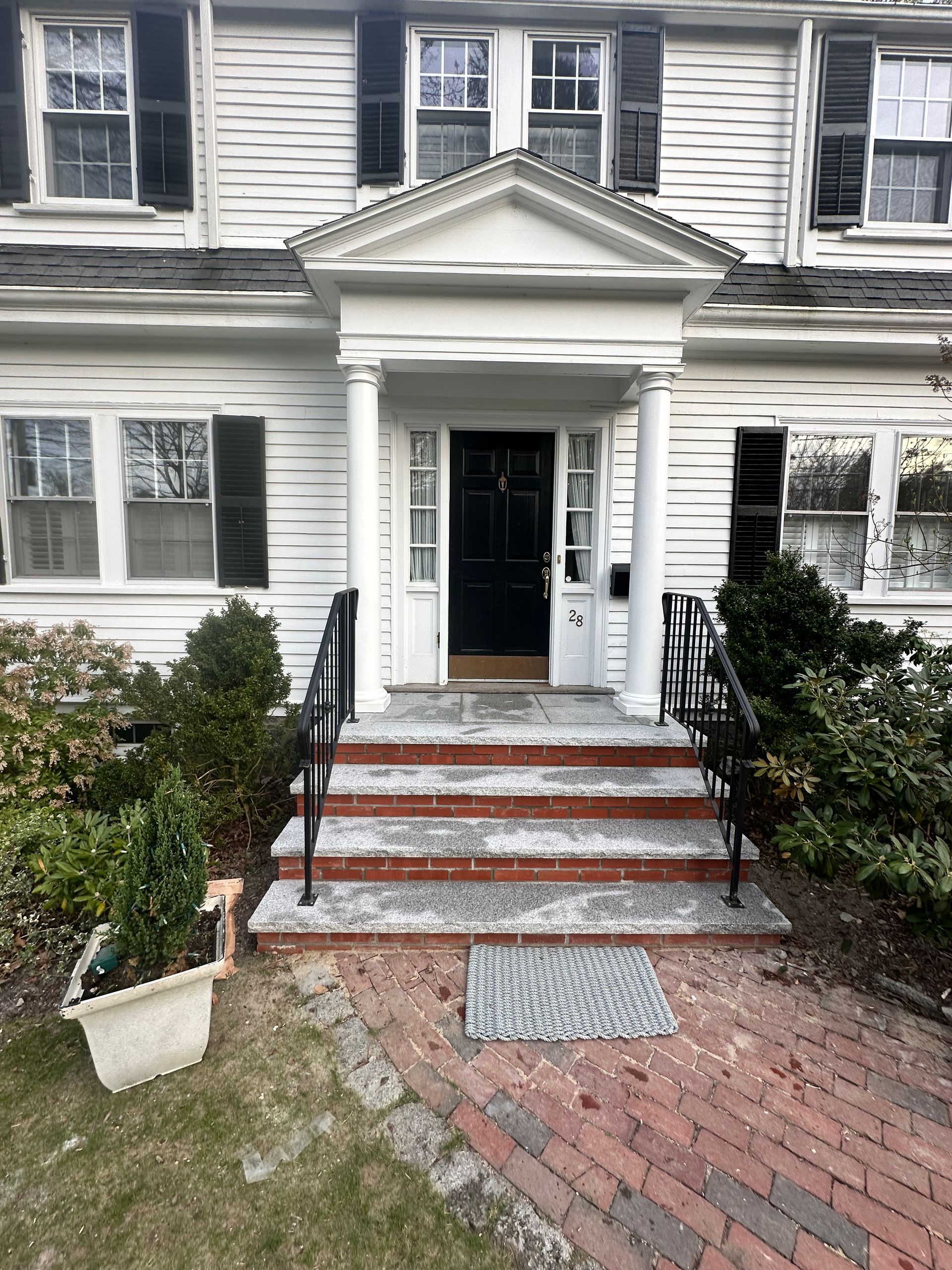 Front entrance of a white house with black shutters, brick walkway, and steps leading to an open door