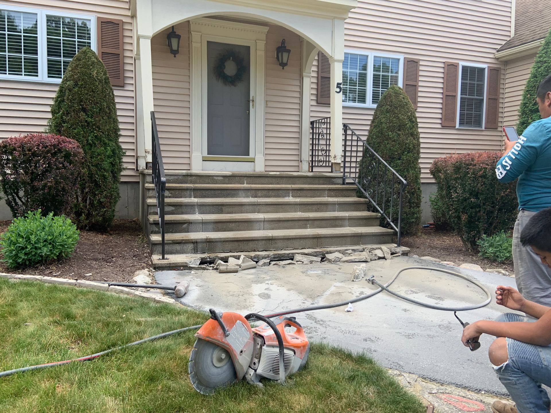 Person power-washing a house entry with a gas pressure washer and hose on the front walkway.