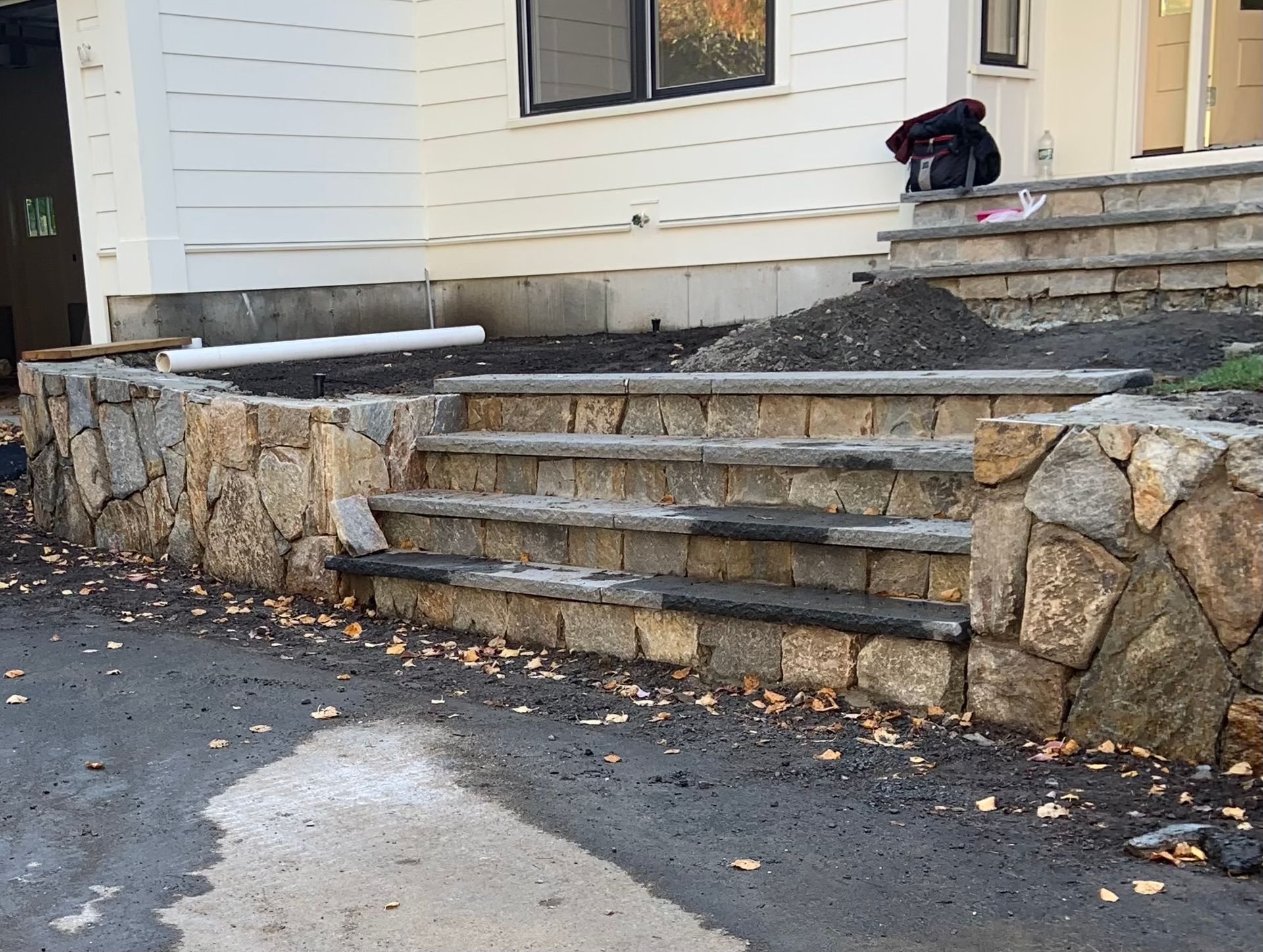 Stone front steps and retaining wall beside a white house entrance, with a black backpack on the stoop.