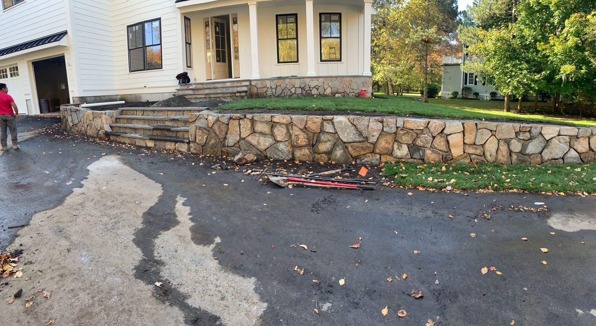 Wet driveway beside a stone retaining wall and house, with scattered debris and a broken red object.