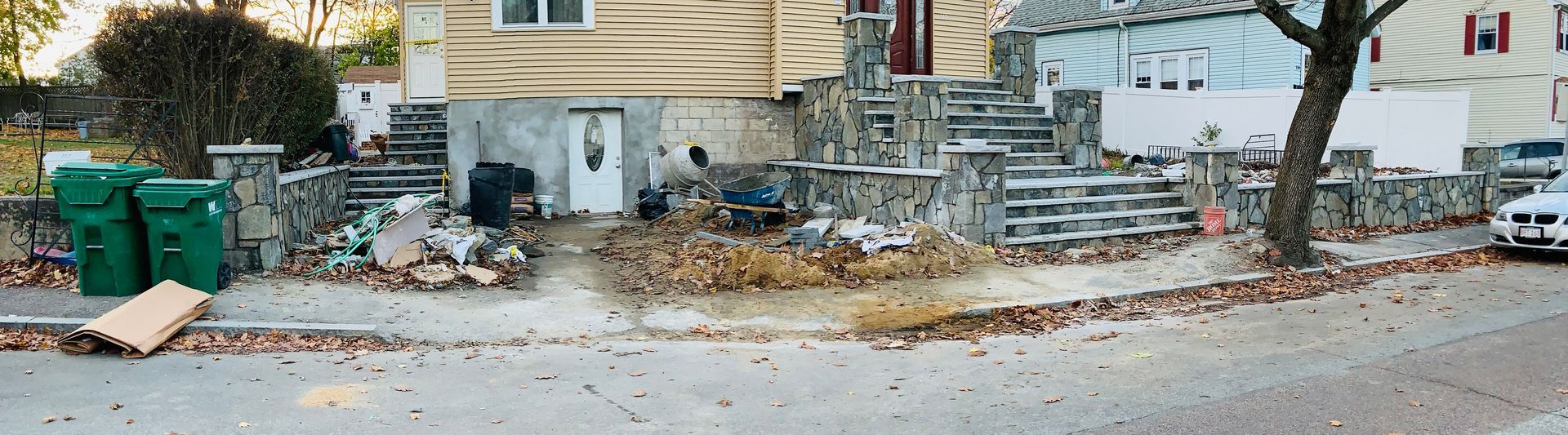 Street scene with rubble and debris beside green trash bins and a damaged building under repair