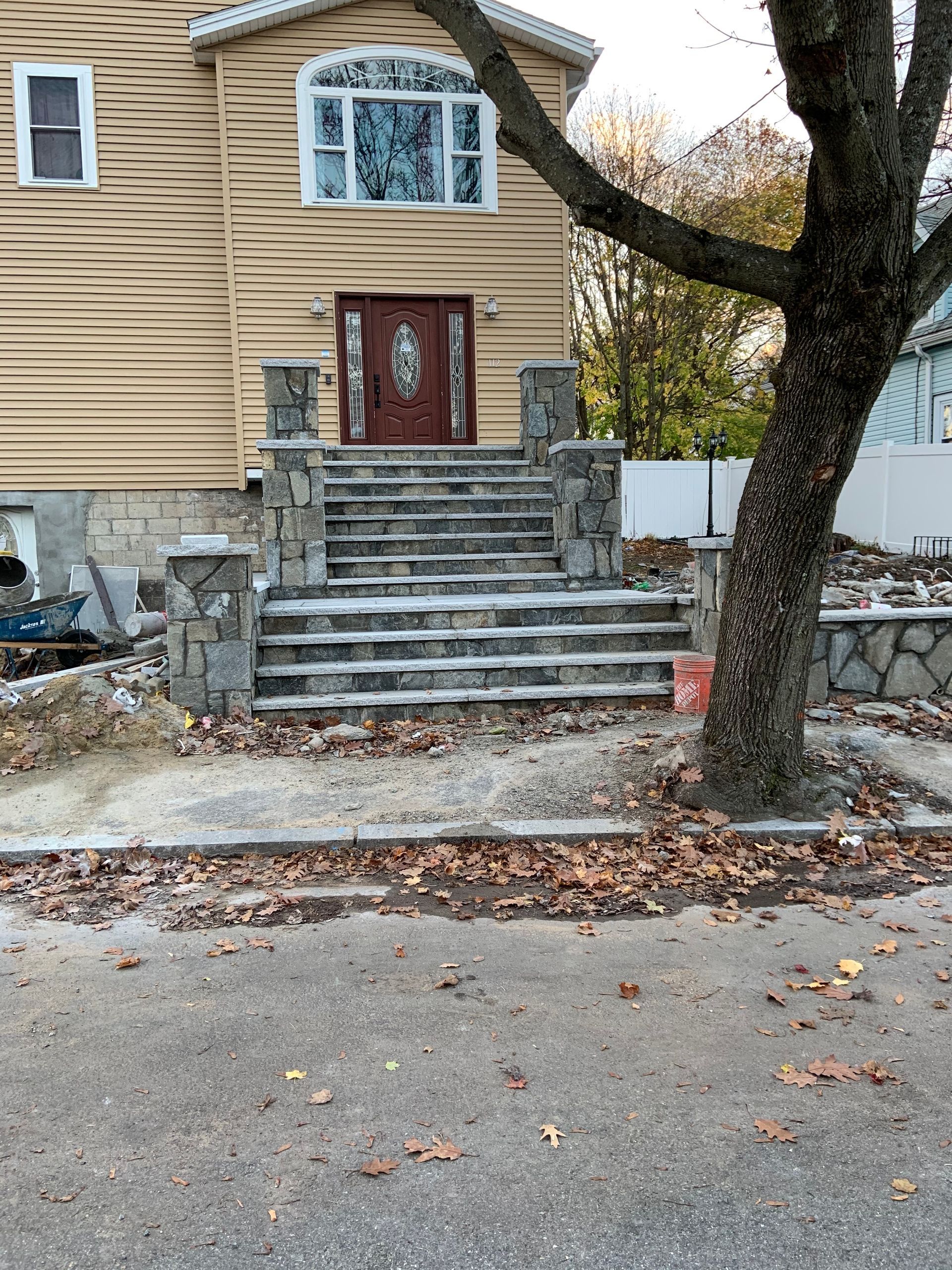 Front steps of a beige house with red door, stone stairs, and a tree in the foreground.