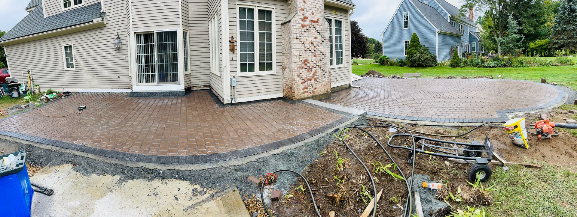 Damaged stone patio and collapsed retaining wall beside a house, with debris and exposed ground.