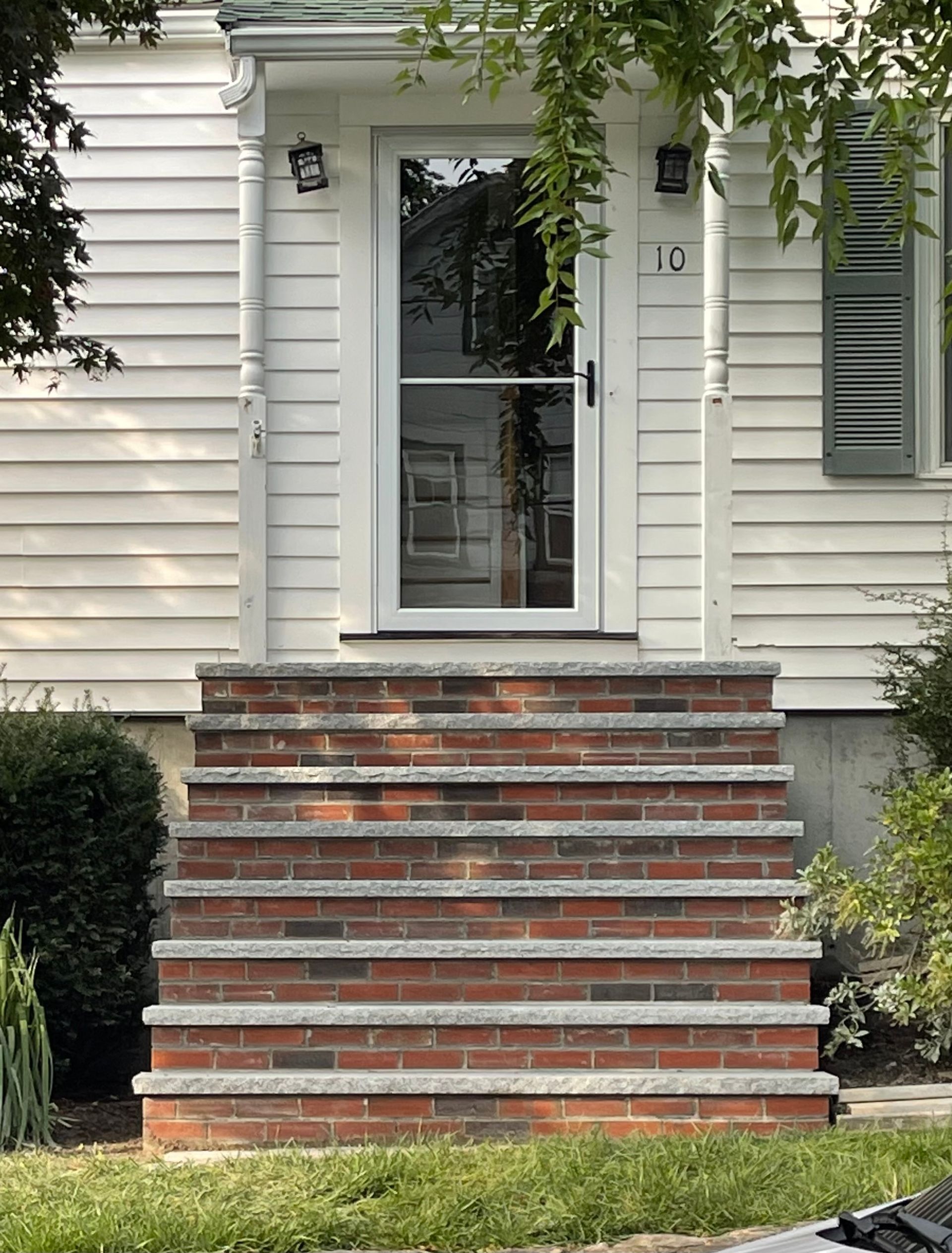 Front steps of a house leading to a white front door with red brick stair treads and siding.
