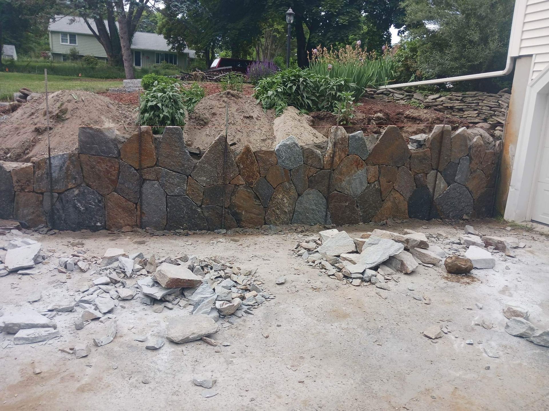 Stone retaining wall with broken concrete debris in a yard near a house