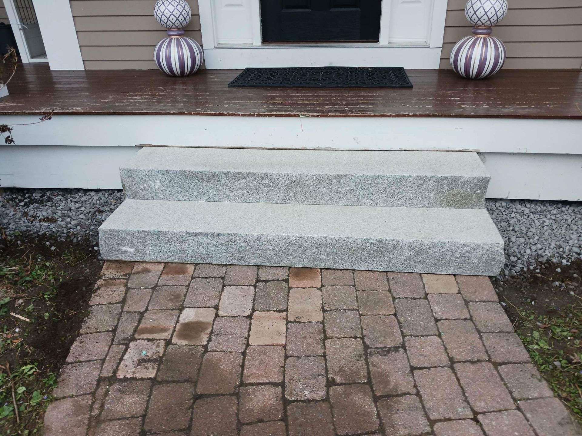 Front porch with three gray concrete steps leading to a brick walkway, flanked by white columns and fall decor.