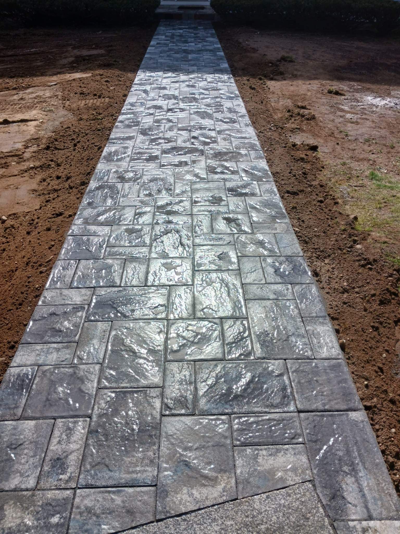 Gray stone walkway leading through a dirt area outdoors.