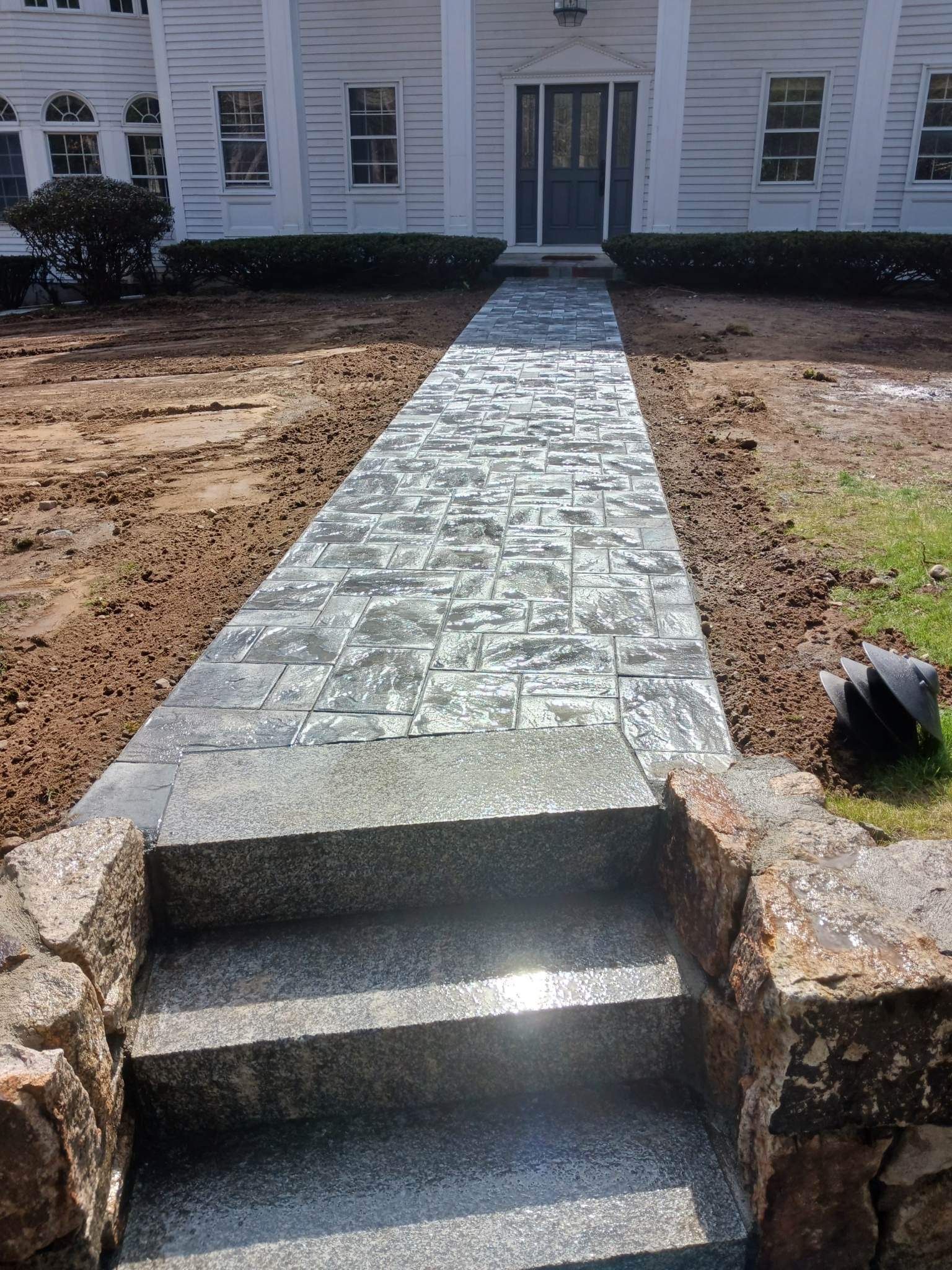 Stone walkway leading to a white house entrance, with short steps and landscaped sides