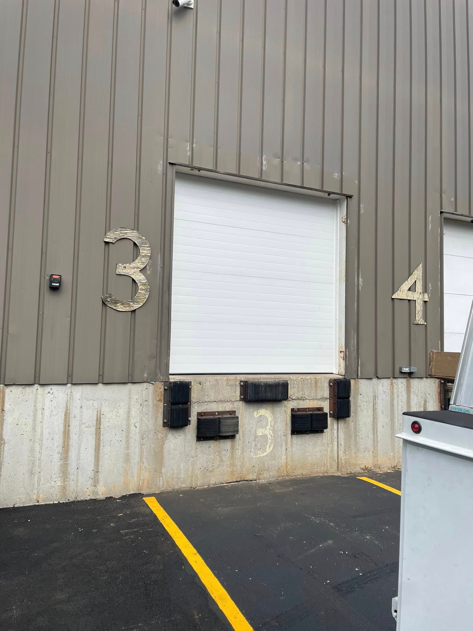 Loading dock entrance numbered 3, with a closed white door, black bumpers, and yellow line.