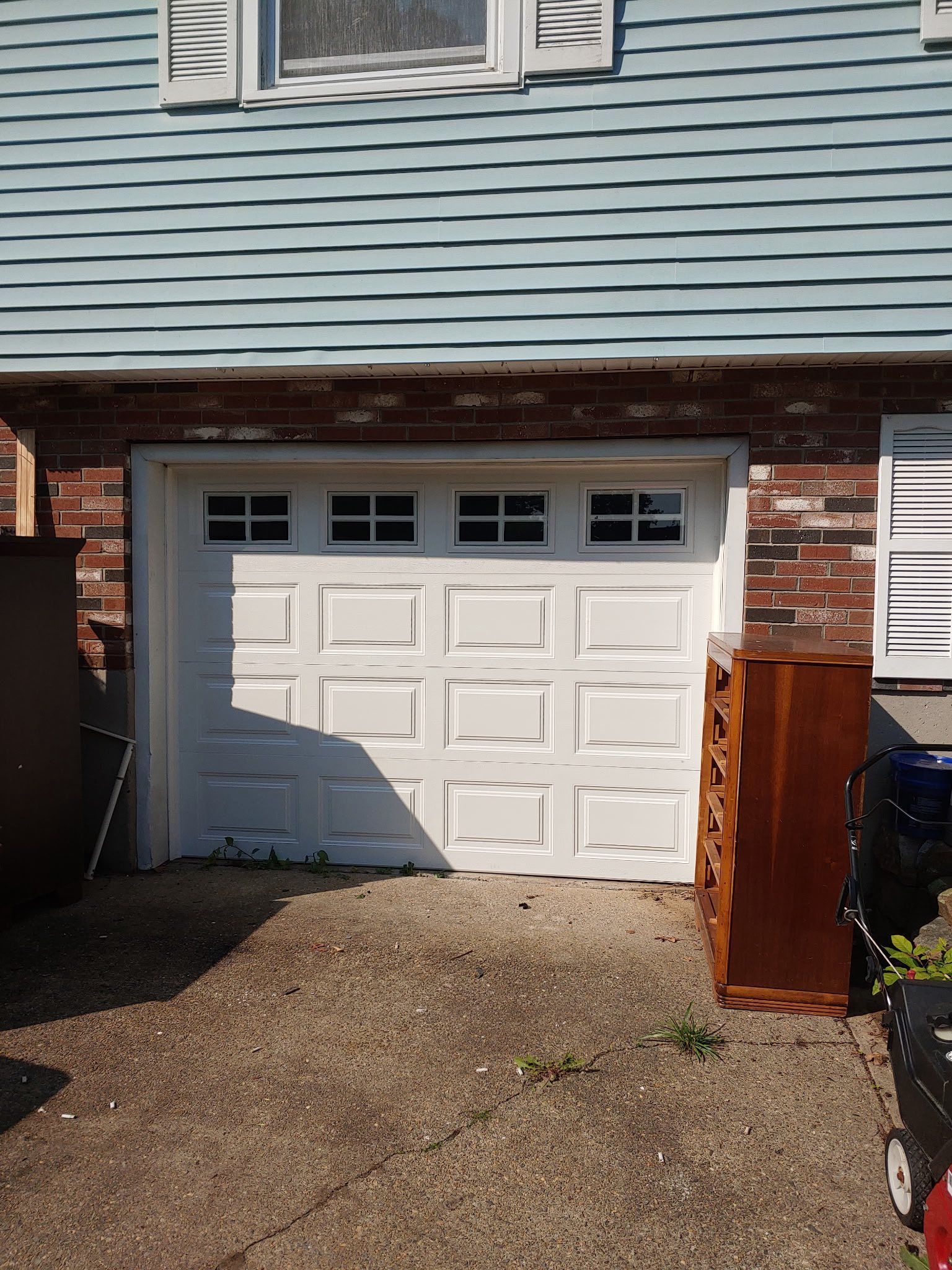 White garage door with glass panel windows above, surrounded by brick and blue siding.