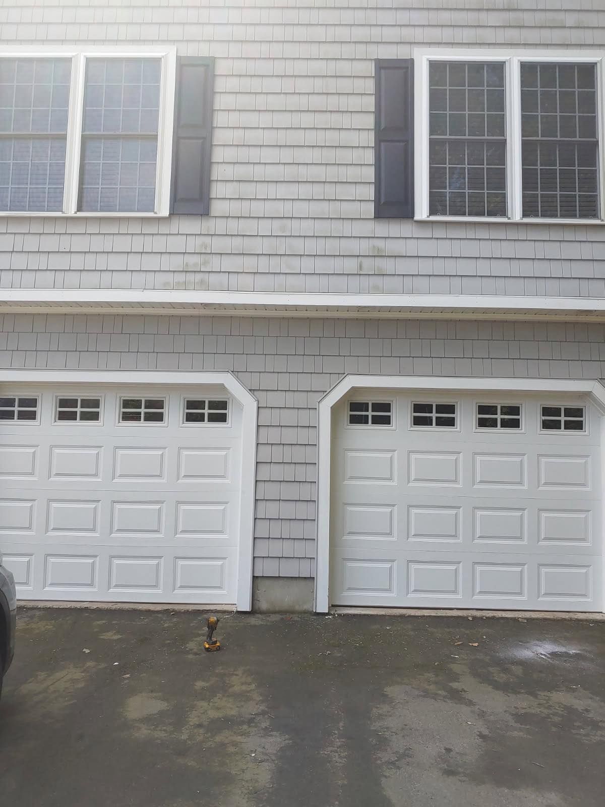 Two white garage doors below two upper windows, gray house exterior.