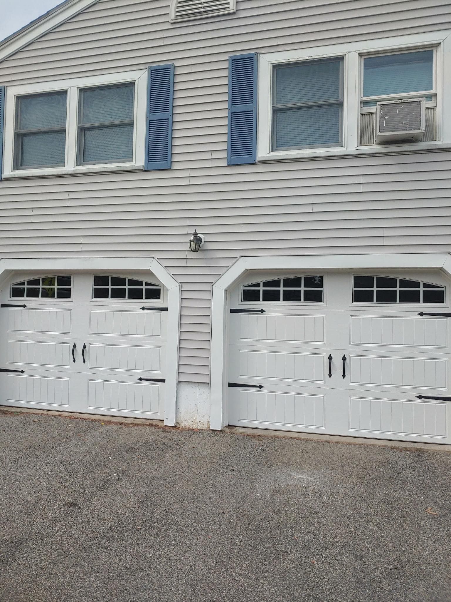 White garage doors with windows, under a light gray house with matching shutters.