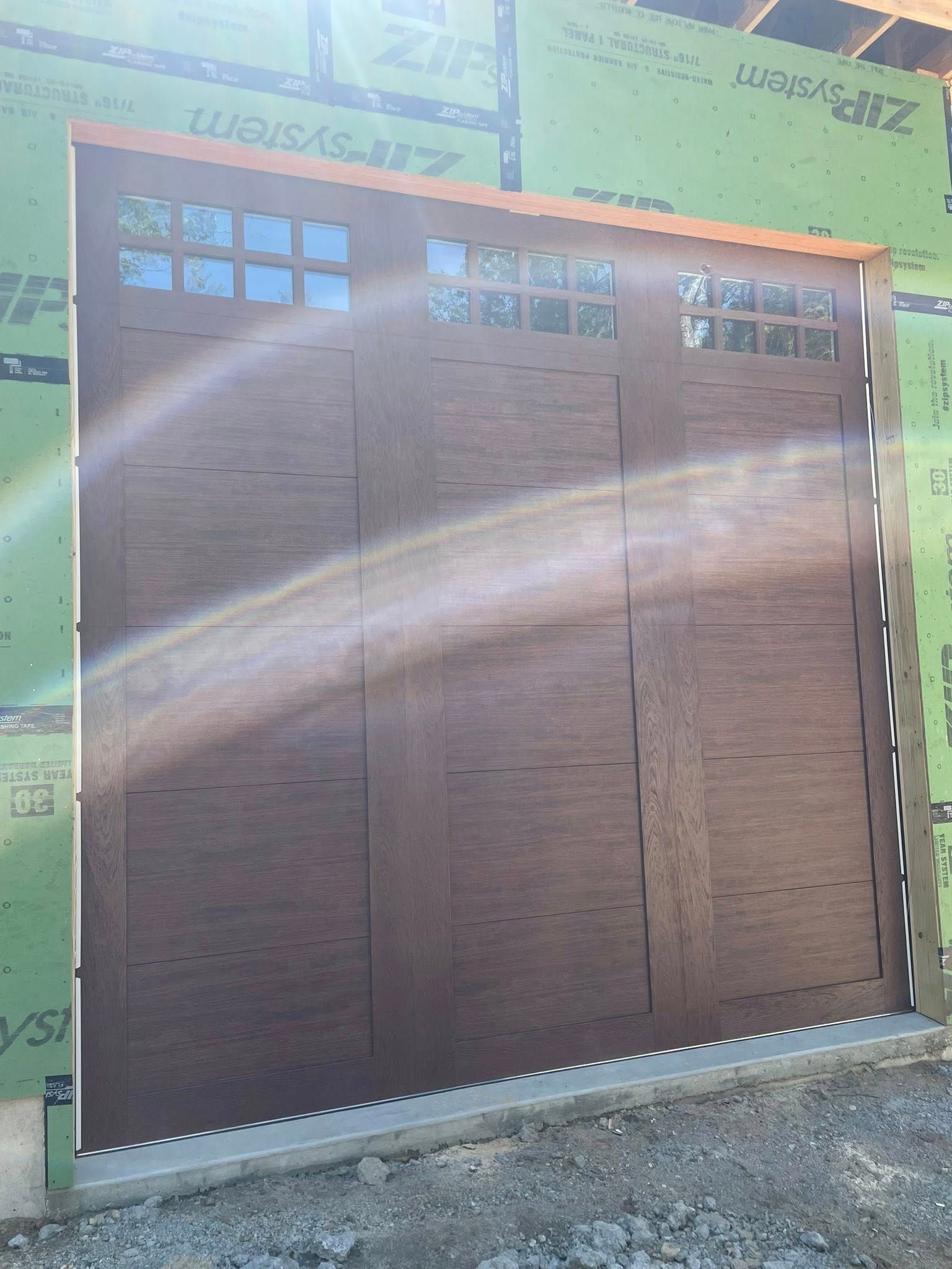 Brown garage door with small square windows; green and wood building under construction.