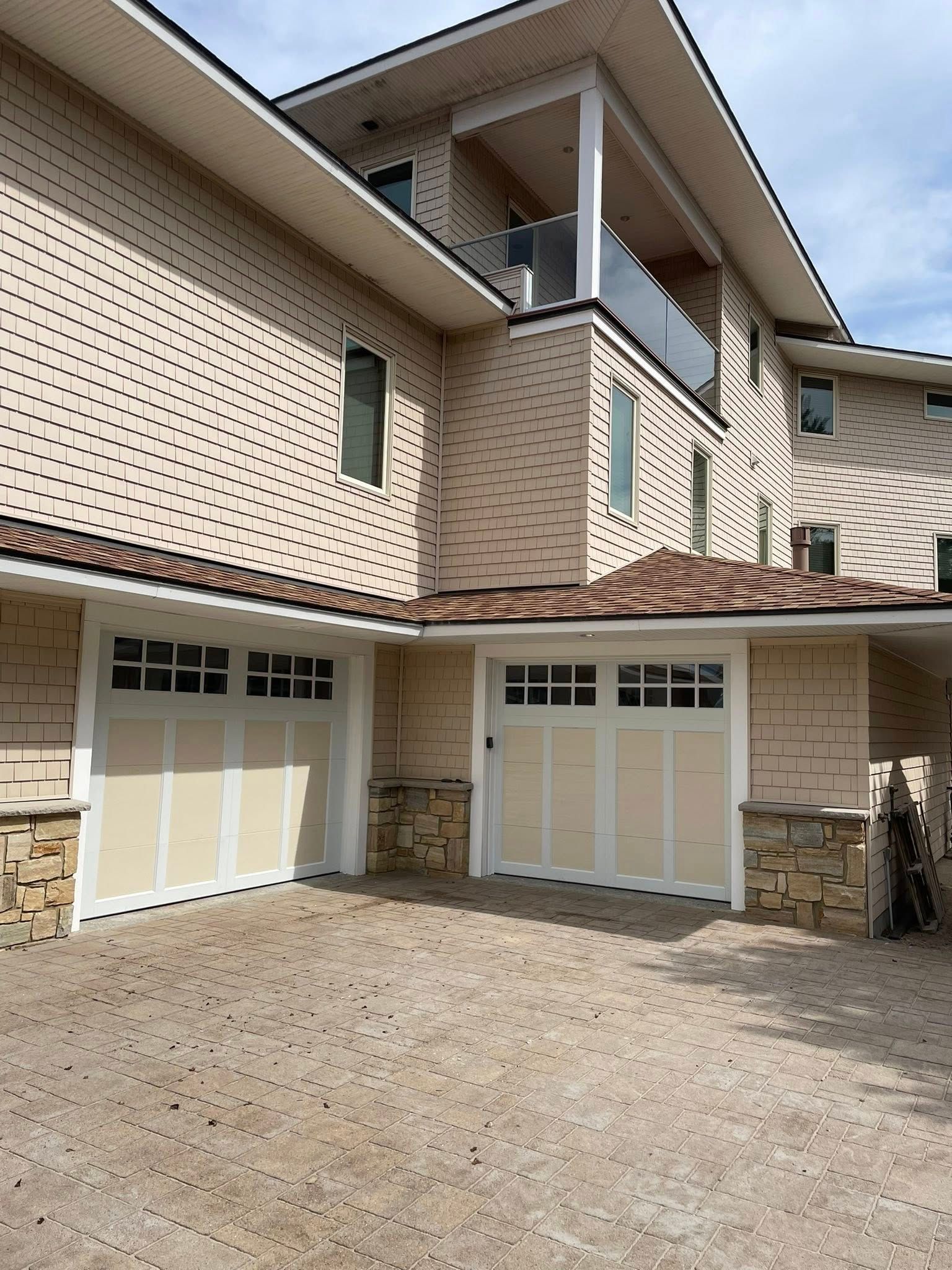 Beige house with light yellow garage doors, stone accents, and a gravel driveway.