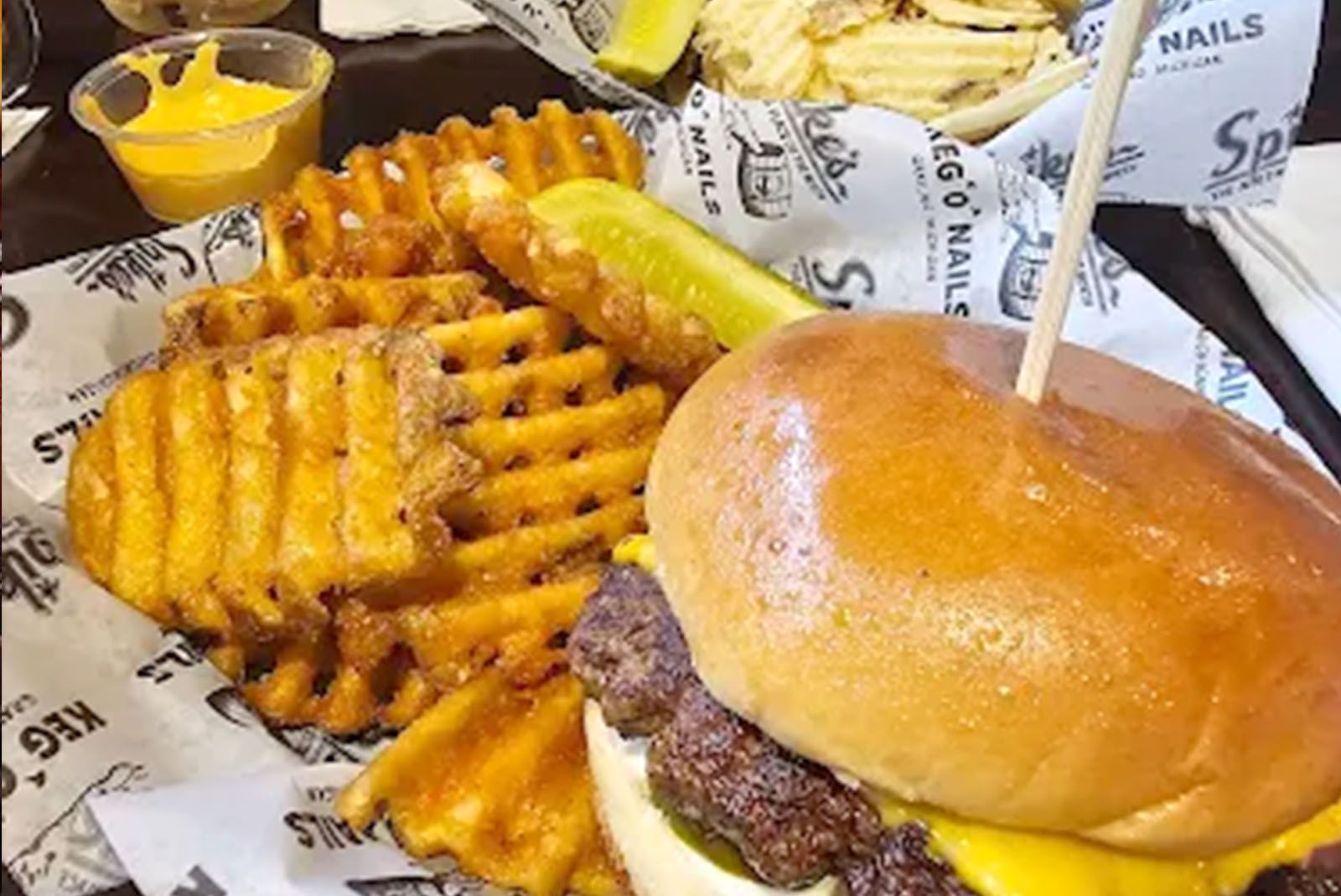 A burger with fries, pickle, and dipping sauce on a basket lined with paper