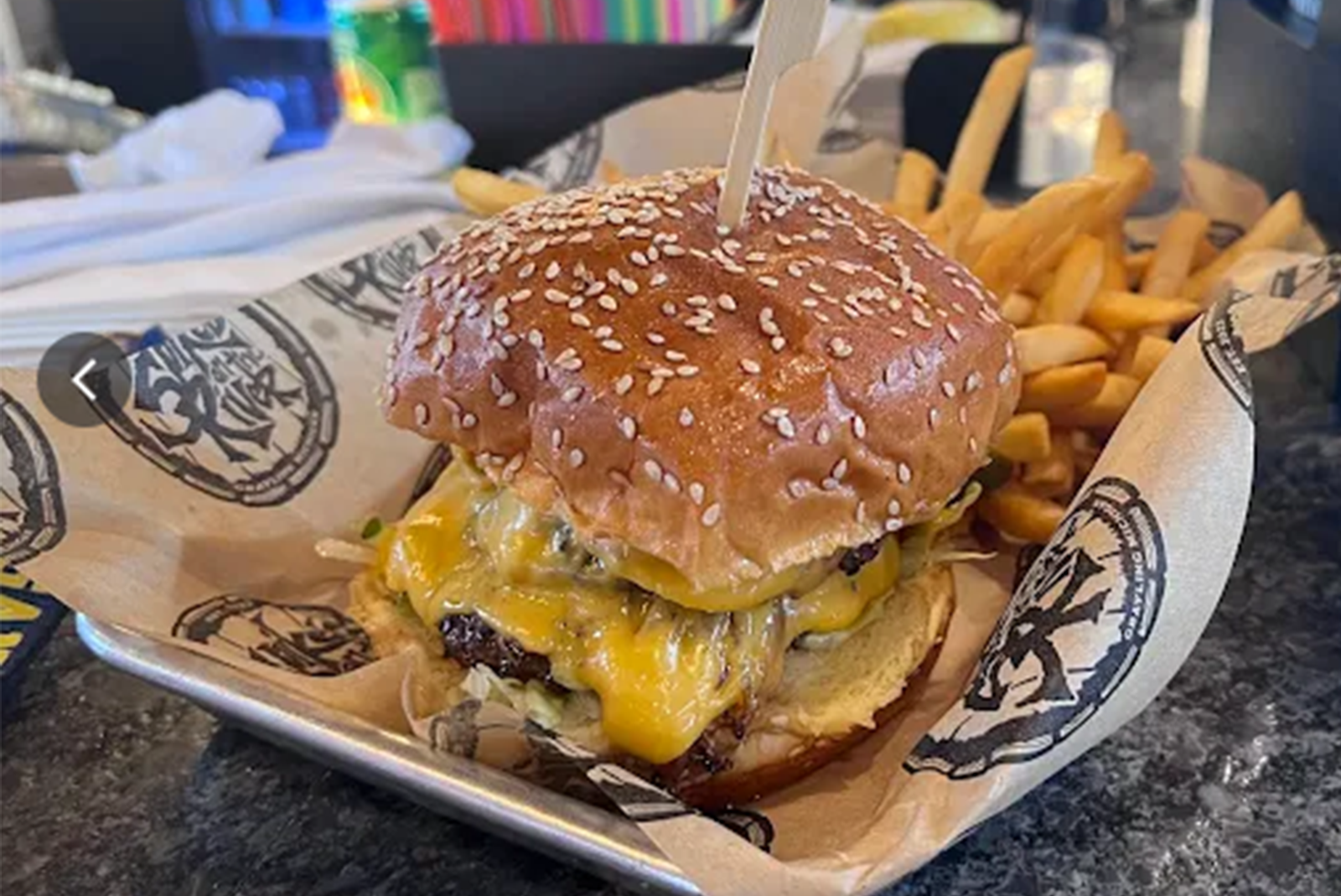 Learn More About Menu A double cheeseburger on a sesame seed bun served in a metal tray with a side of french fries.