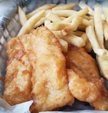 A close-up view of golden-brown fried fish fillets served alongside a portion of thin-cut French fries in a food basket. 