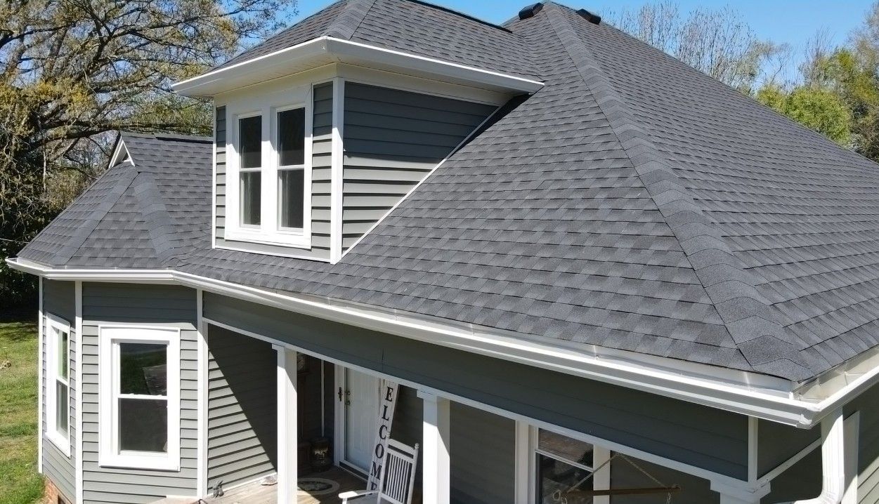 Gray house with white trim, dark roof, windows, and porch in daylight.