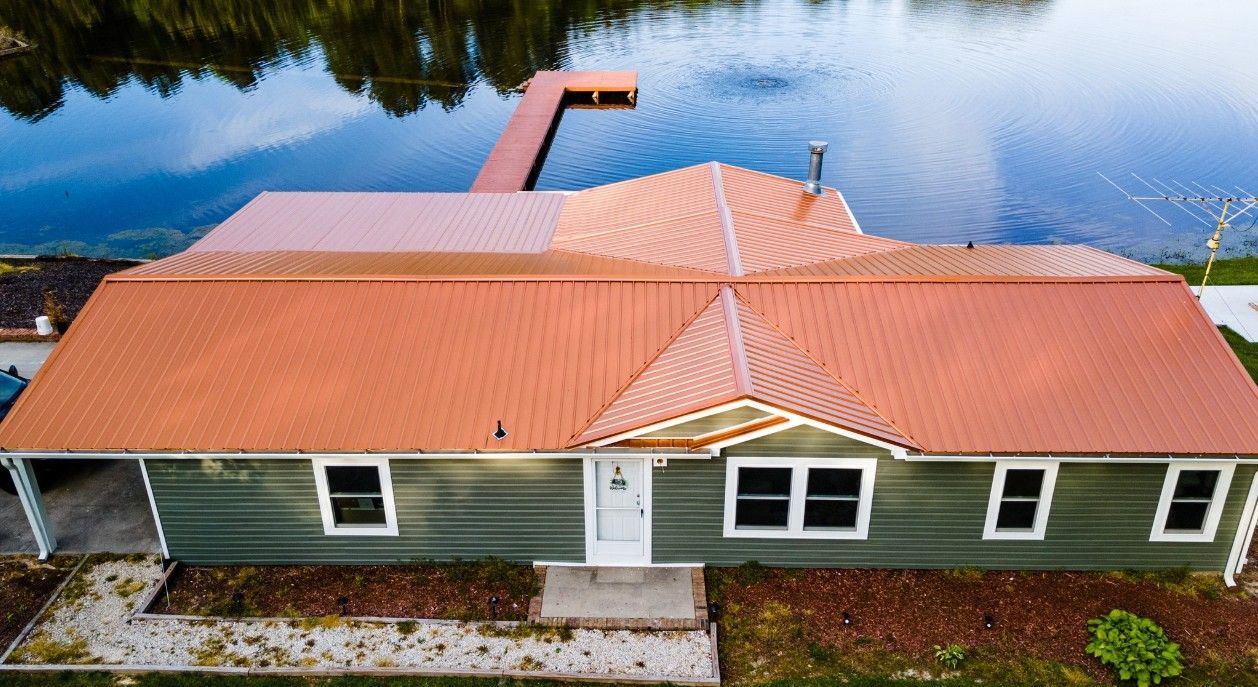 Green house with orange roof, lakeside dock in the distance.