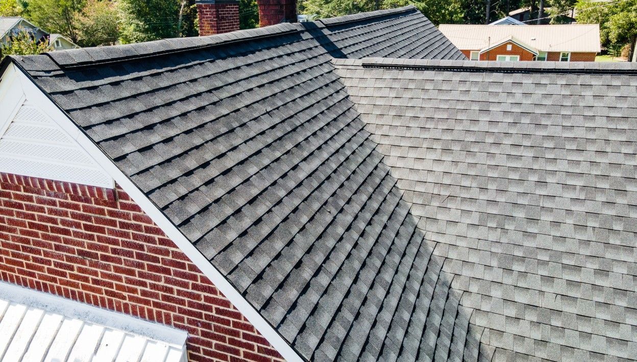 Gray asphalt shingle roof on a brick house with a chimney under a sunny sky.