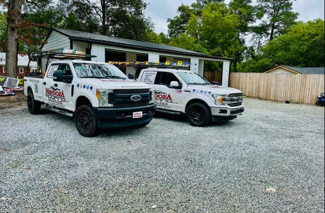 Two white work trucks with company logos parked in front of a building with gravel parking.