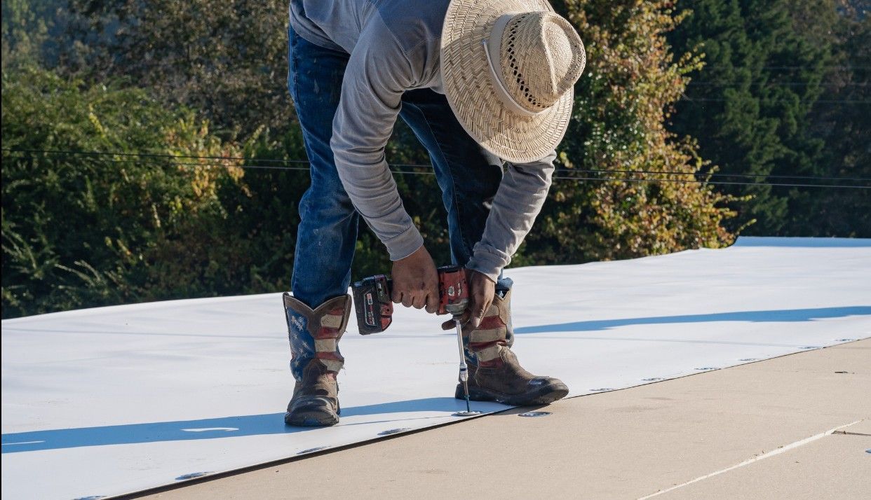 Man in cowboy boots using a drill on a white surface outdoors, wearing a straw hat.