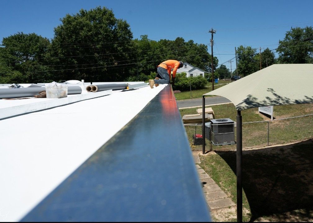 Man in orange vest works on a metal roof edge on a sunny day.