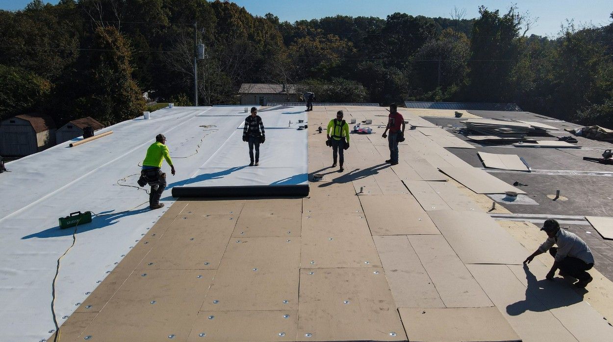Roofing crew installing layers on a flat roof, with sunlight.