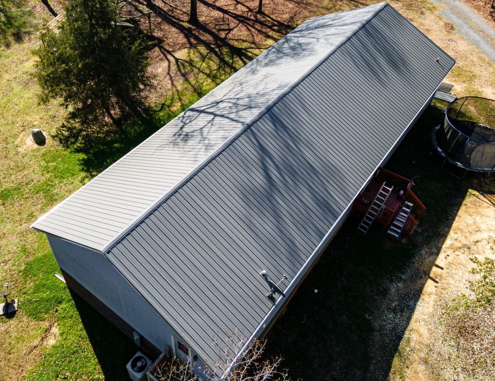Aerial view of a gray metal roof on a building, with a small deck and grassy surroundings.