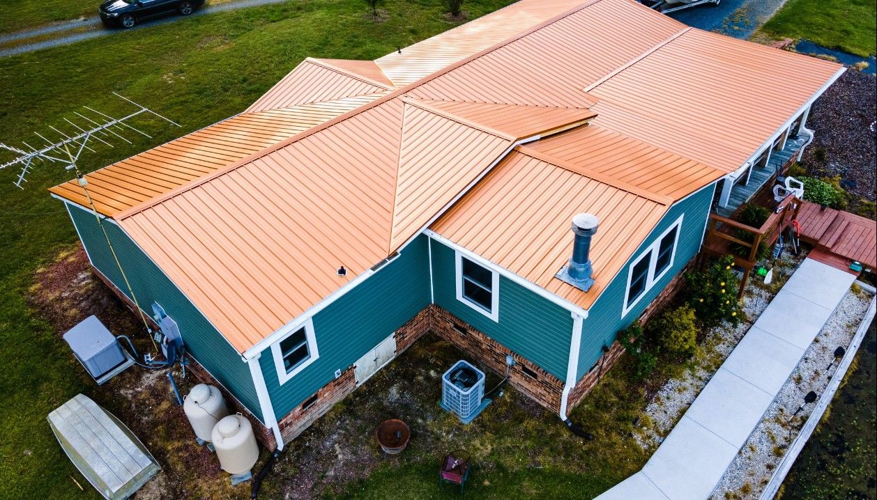 Aerial view of a teal house with an orange metal roof, white trim, and a concrete walkway.