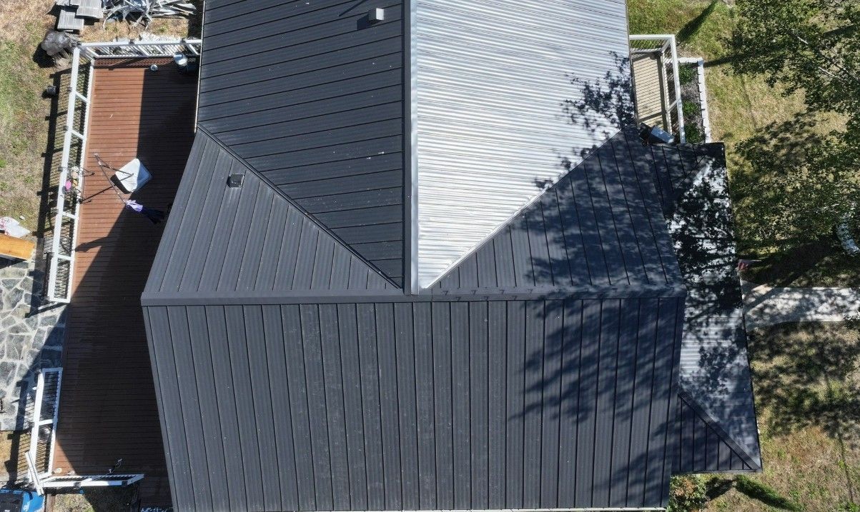 Overhead view of a dark gray shingled roof on a house with a deck and trees.