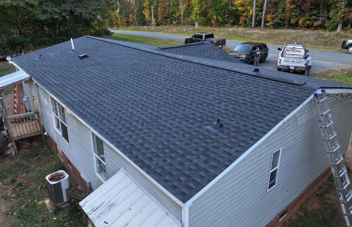 Gray house with a newly shingled, dark gray roof, vehicles parked on the road behind it.