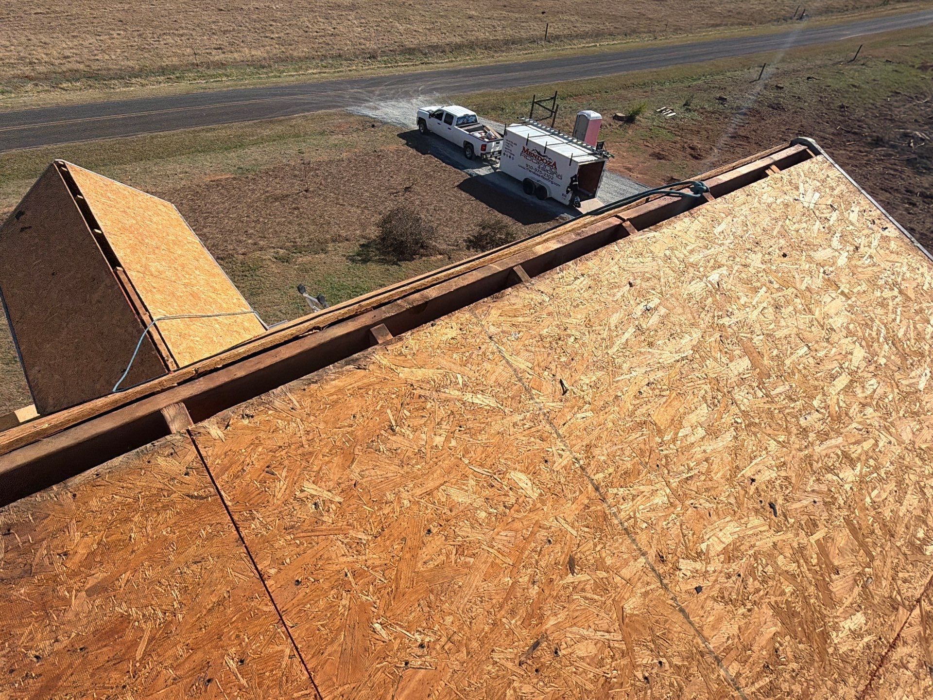 Unfinished roof with wood sheathing; vehicles parked on asphalt driveway.